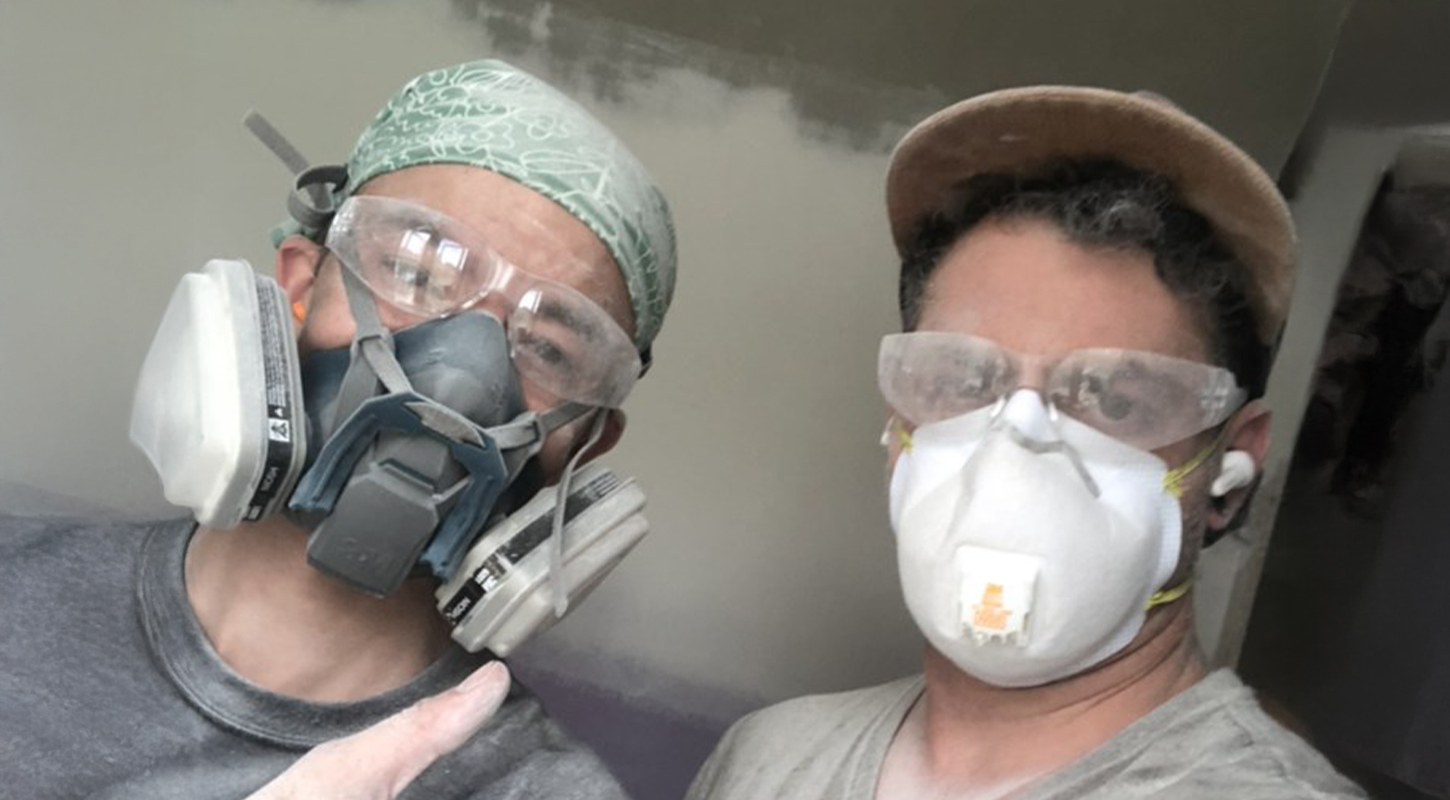 Two Cleary Team members working on house posing while wearing masks covered in drywall dust