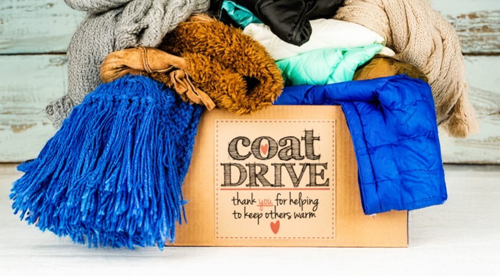 cardboard box with the words "Coat Drive" on the front filled with coats